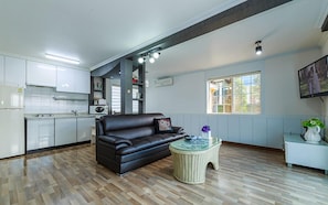 A modern living space with a black leather sofa, a wicker coffee table, and a kitchen area with white cabinets and a microwave. - Morning Lake Pension (Pocheon)