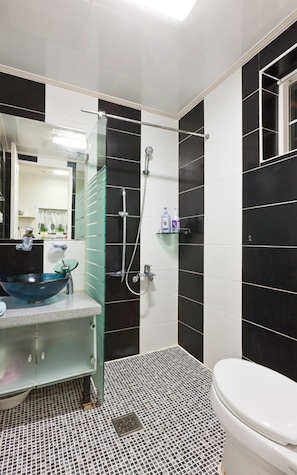 A bathroom with a black and white tiled wall, a glass shower enclosure, a sink with a blue basin, and a toilet. - Morning Lake Pension (Pocheon)