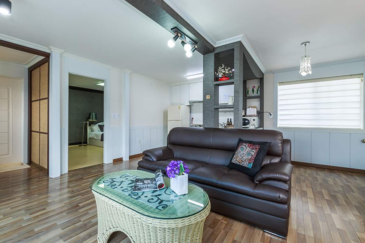 A living room with a brown leather sofa, a glass coffee table with a woven base, and a chandelier.