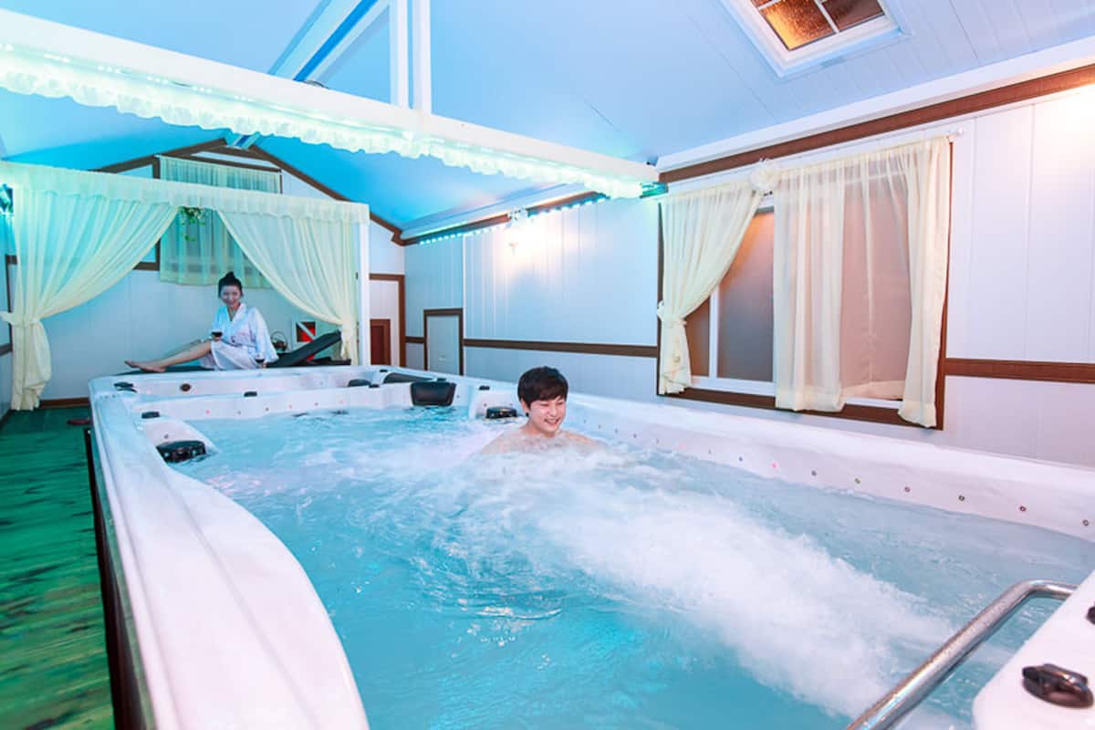 A room with a large hot tub, a bed, and a window with curtains.