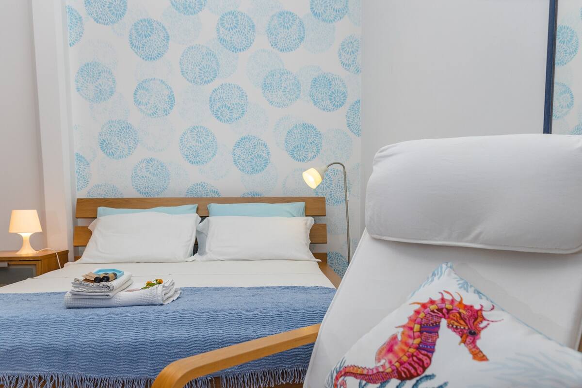 A hotel room with a bed, a chair, a nightstand, and a wall with a circular pattern.