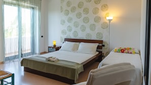 Hotellihuone, jossa on sänky, yöpöytä lampun kanssa, tuoli ja ikkuna, jossa on ohuet verhot.