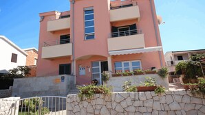 Un edificio de dos pisos con fachada rosa, balcones y un muro de piedra frontal.