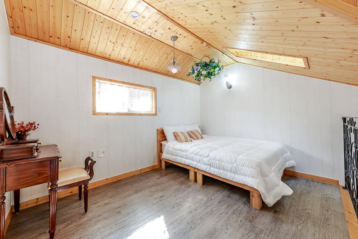 Ein Schlafzimmer mit Holzbalkendecke, einem Bett, einem Schreibtisch mit Stuhl und einem Fenster.