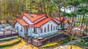 A two-story house with a red-tiled roof, a swimming pool, and a wooden deck. - Lake and Pine Spa Pension (Pocheon)