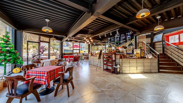 An indoor dining area with wooden tables and chairs, a Christmas tree, and a menu board. - Lake and Pine Spa Pension (Pocheon)