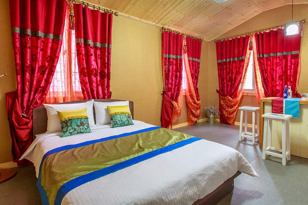 Ein Schlafzimmer mit einem Bett, zwei Nachttischen, einem Schreibtisch und roten Vorhängen.