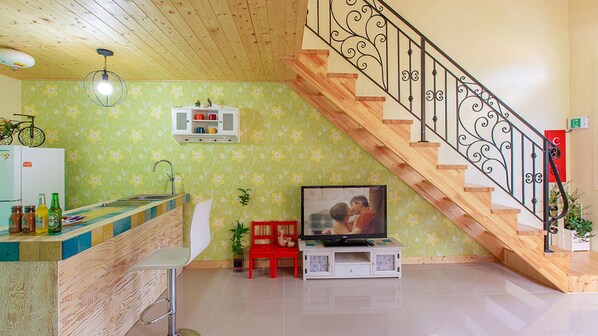 Uma sala de estar com escada de madeira, televisão, espaço de cozinha e parede estampada.