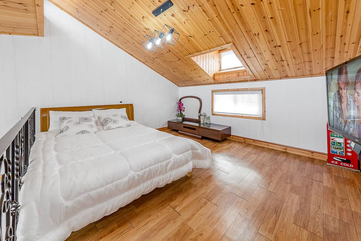 Ein Schlafzimmer mit Holzbalkendecke, einem Bett mit weißer Bettwäsche, einem Schminktisch, einem Spiegel, einem Fenster und einem Fernseher.