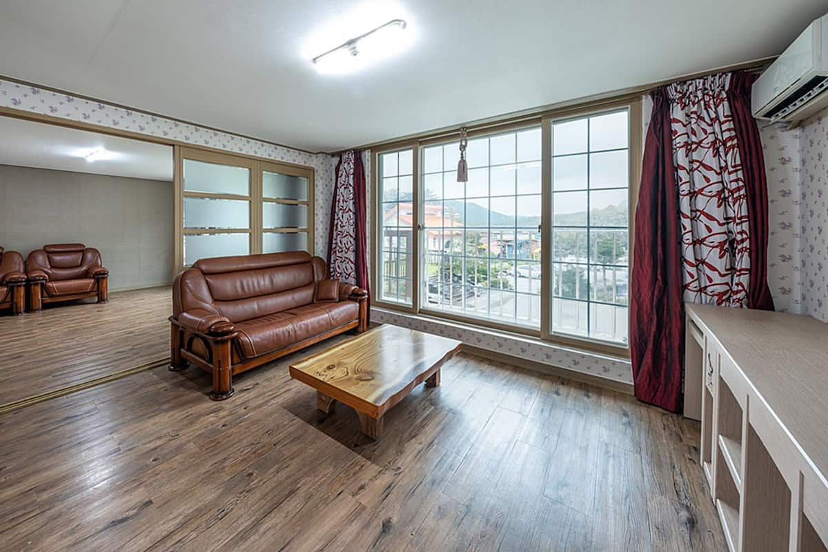 Ein großzügiger Wohnraum mit einer braunen Ledersofa, zwei Sesseln und einem Holztisch. Große Fenster bieten Blick auf die Stadtlandschaft.