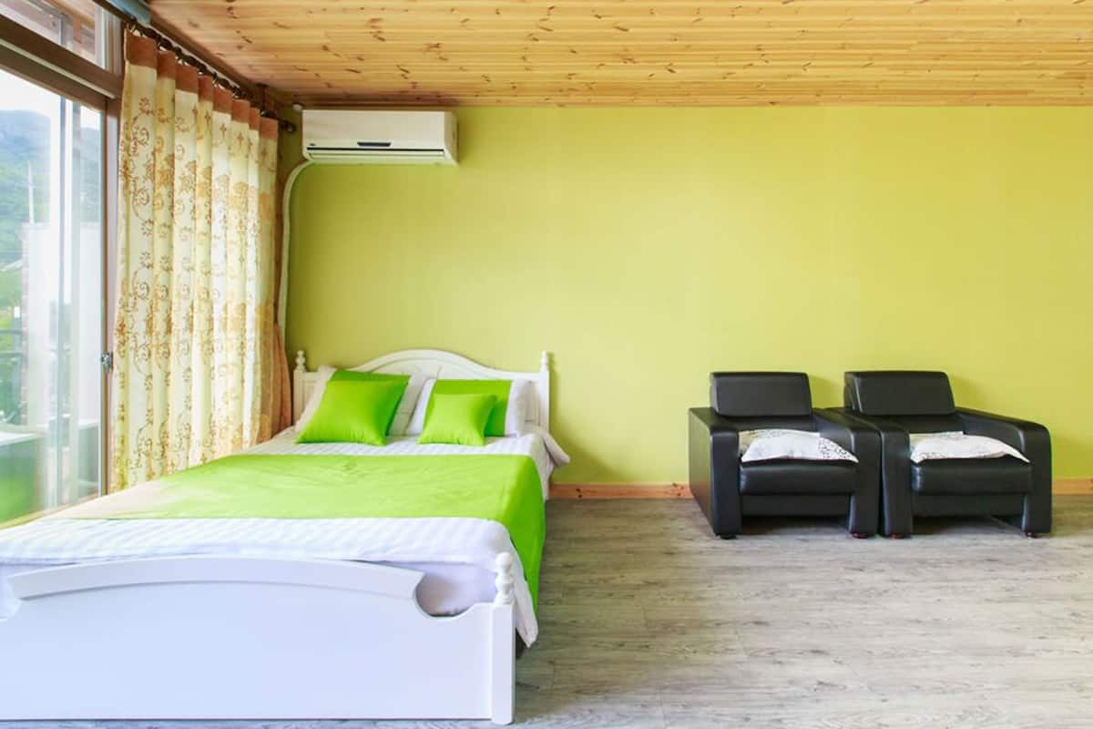 Ein Schlafzimmer mit einem Bett, zwei Stühlen und einem Fenster mit Vorhängen.