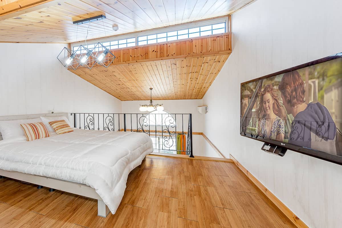 Ein Schlafzimmer mit Bett, Holzboden, einem an der Wand befestigten Fernseher und einem Balkon mit Geländer.