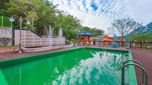 A swimming pool with a water fountain, a gazebo, and outdoor seating. - Lake and Pine Spa Pension (Pocheon)