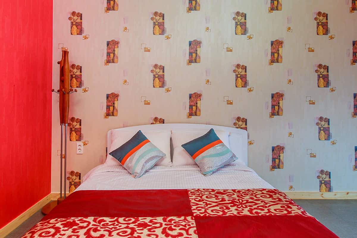 Ein Zimmer mit einem Bett, roten Wänden und ornamentalem Wandpapier.