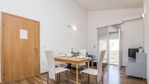 Un comedor con una mesa de madera, cuatro sillas, un televisor y un gran ventanal corredera que da a un espacio exterior.