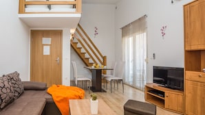 Un espacio habitable compacto con sofá, mesa de comedor, televisor y escalera.