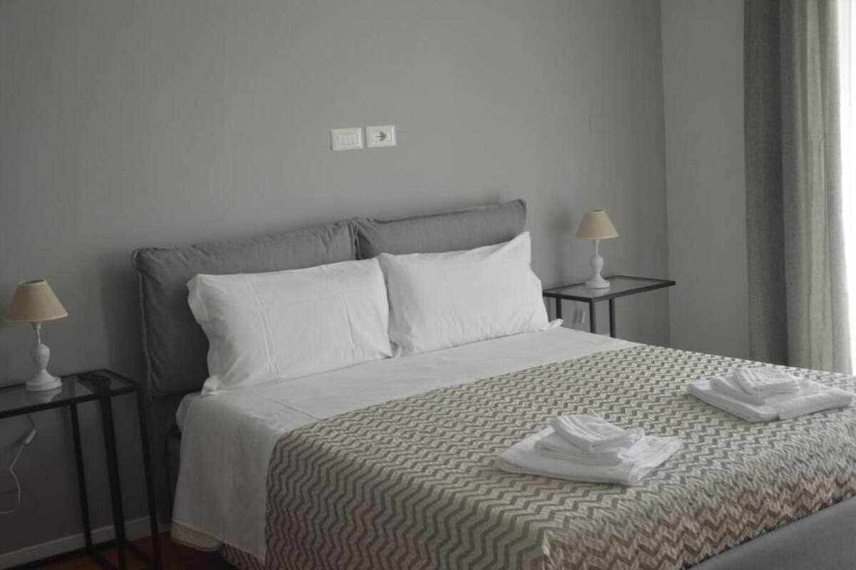 A hotel room with a bed, two bedside tables, a lamp on each table, and a window with curtains.