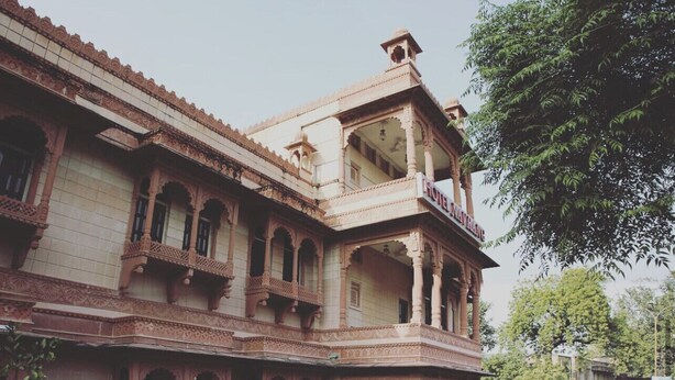 Un edificio histórico con arquitectura ornamentada, un patio a cuadros y un césped verde.