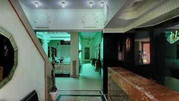 A hotel lobby with a marble reception desk, a staircase, and a green-lit corridor.
