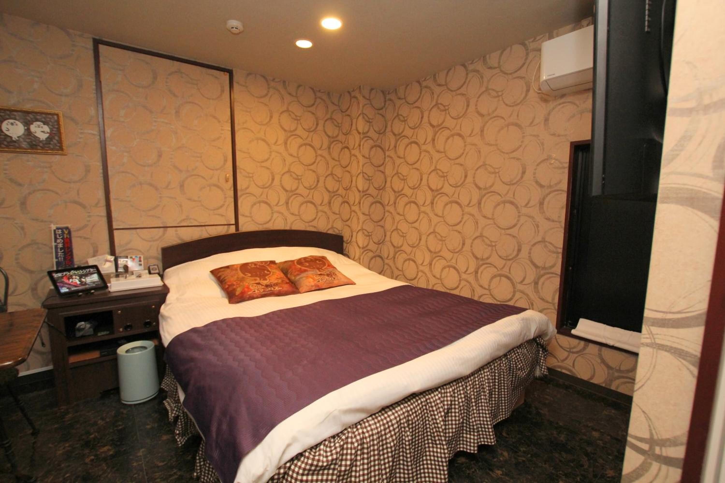 A hotel room with a bed, a nightstand, a trash bin, and a wall-mounted air conditioner.