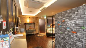 A hotel reception area with a PayPay sign, a waiting room sign on a brick wall, and a refrigerator in the background. - Hotel GOMAX - Adults Only (Yokohama)