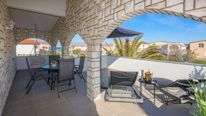 A covered outdoor area with stone pillars, a table with chairs, and a lounge chair. - Apartments Bojana (Vir)