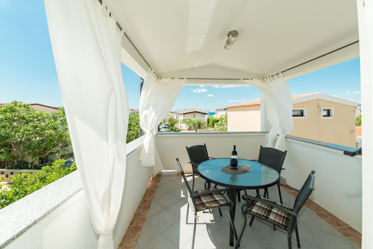 Un balcon extérieur abrité, doté d’une table ronde et de quatre chaises, qui offre une vue sur un quartier résidentiel avec ses maisons et sa verdure.