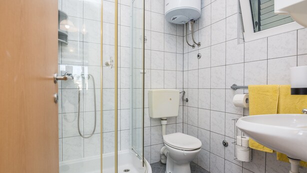 A bathroom with a glass-enclosed shower, a toilet, and a sink with a yellow towel. - Apartments Bojana (Vir)