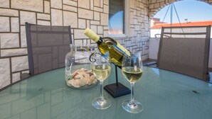 A glass table with two wine glasses, a bottle of wine, and a glass jar of seashells. - Apartments Bojana (Vir)