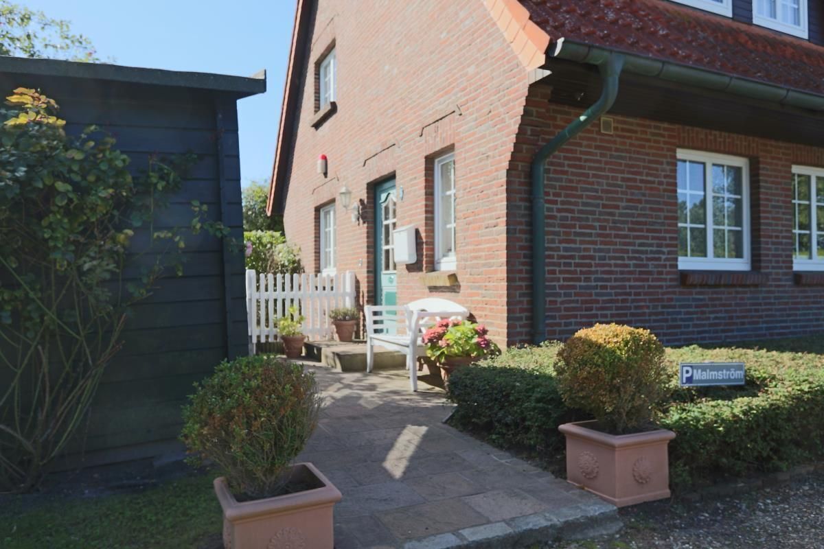 Ein Backsteinhaus mit einer kleinen Veranda, einem weißen Stuhl und Topfpflanzen.
