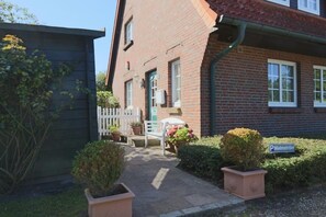 A brick house with a small porch, a white chair, and potted plants. - Sylt at home, Germany (Sylt-Ost)