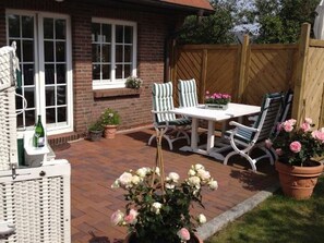 A patio with a table and chairs, surrounded by potted plants and a wooden fence. - Sylt at home, Germany (Sylt-Ost)