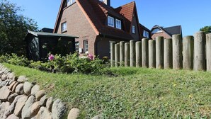 A traditional brick house with a sloped roof, a wooden fence, and a stone wall in the foreground. - Sylt at home, Germany (Sylt-Ost)