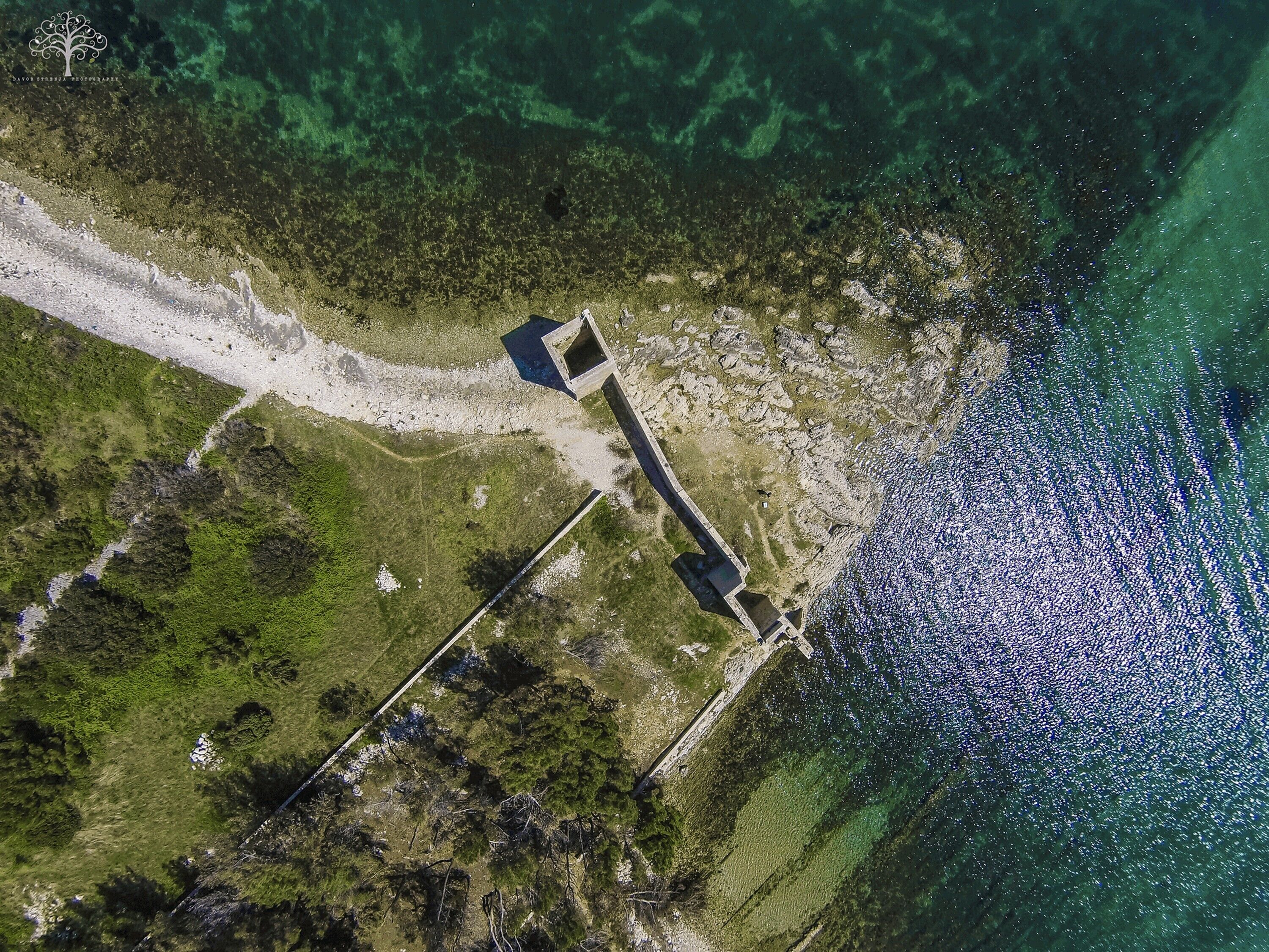 An aerial view of a coastal property with a long, narrow building adjacent to a sandy beach and a clear blue sea.