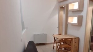 Un espace de vie compact comprenant un canapé noir, une table à manger en bois avec des chaises et un radiateur blanc.