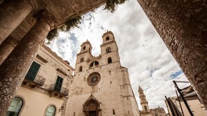 A historic church with a large central dome and two bell towers, surrounded by stone buildings with arched windows. - La Colomba B&B (Altamura)