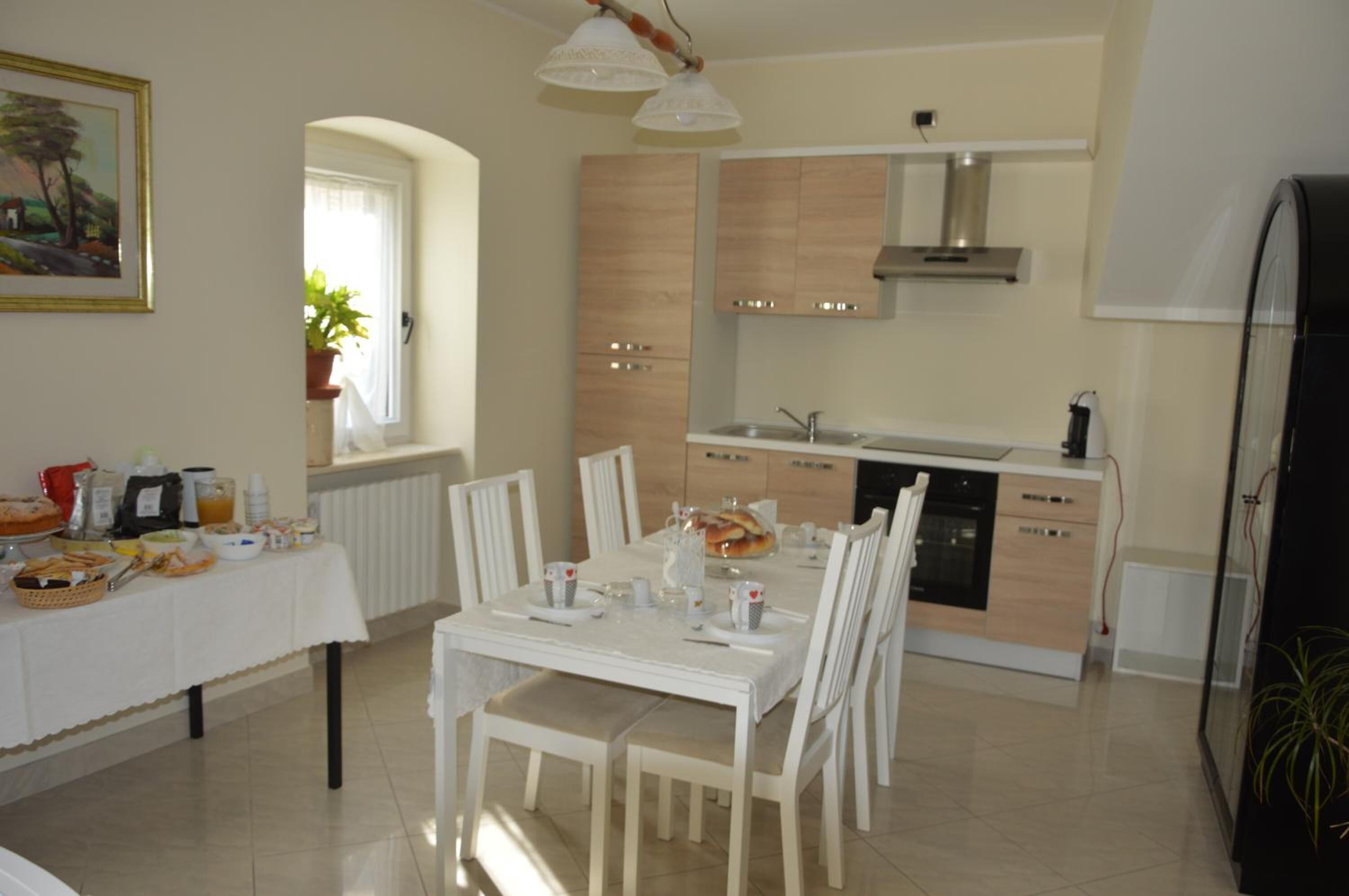 Una cocina moderna con gabinetes blancos, horno empotrado y comedor con una mesa blanca para cuatro.