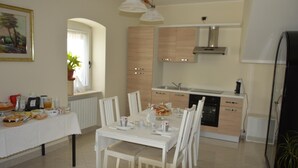 A modern kitchen with white cabinets, a built-in oven, and a dining area with a white table set for four. - La Colomba B&B (Altamura)