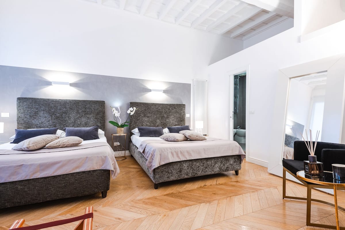 A modern hotel room with two beds, a sitting area with a table, and a large mirror.