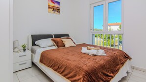 A bedroom with a bed, a nightstand, a lamp, and a window with a view of greenery. - Apartment Andreja (Vir)