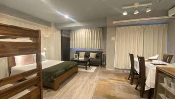 A modern hotel room with a bunk bed, a sofa, a dining table with chairs, and a large window with curtains.