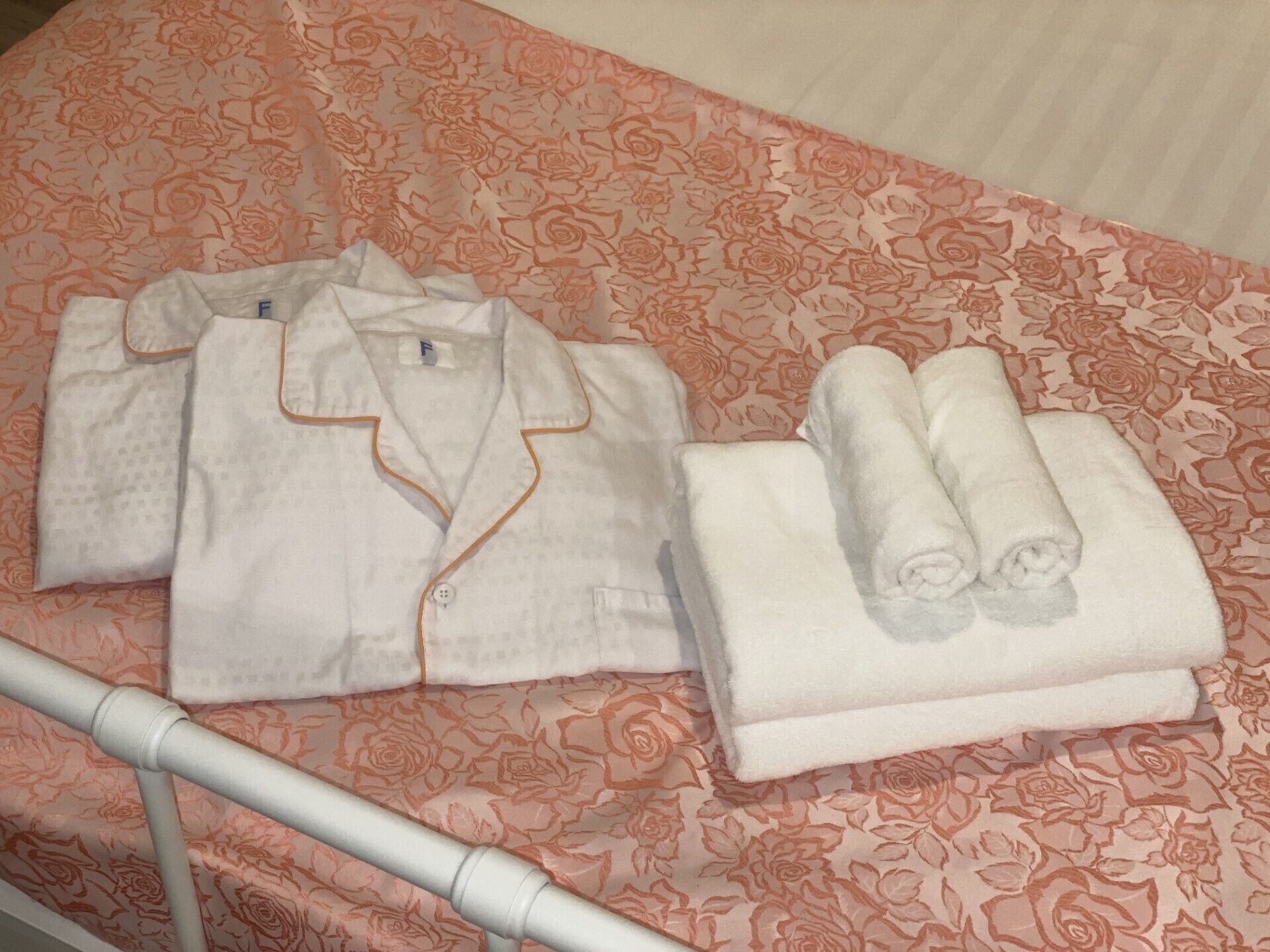 A neatly folded white shirt and two rolled-up towels on a bed with a floral-patterned bedspread.