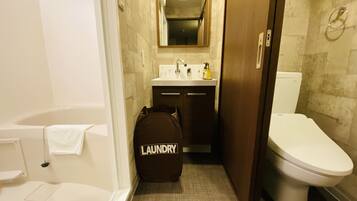Une petite salle de bain comprenant une baignoire, des toilettes et un lavabo. Un sac à linge est posé sur le sol.