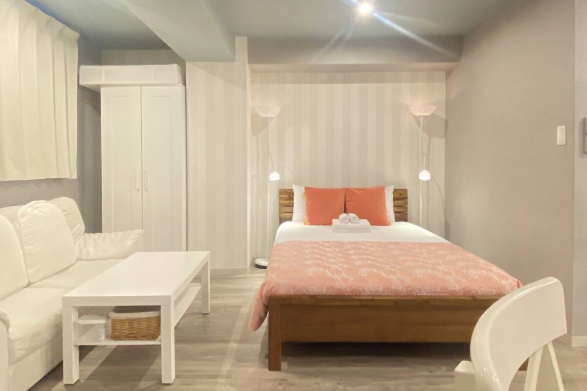 A bedroom with a bed, a bedside table, a chair, a wardrobe, and a window with curtains.