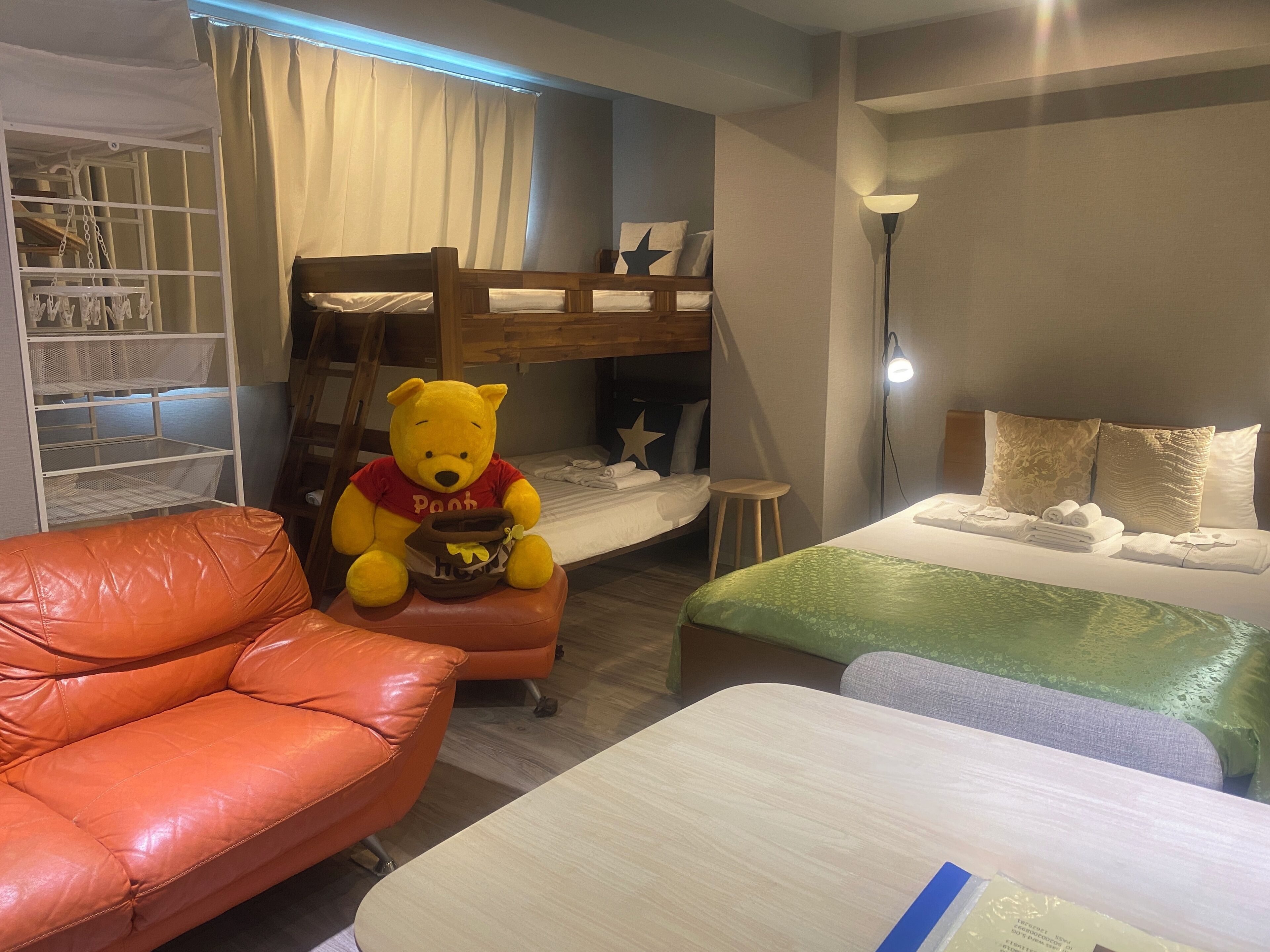 A cozy room with a bunk bed, a plush orange leather sofa, a large Winnie the Pooh stuffed toy, and a bedside table with neatly folded towels.