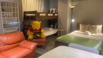 A cozy room with a bunk bed, a plush orange leather sofa, a large Winnie the Pooh stuffed toy, and a bedside table with neatly folded towels.