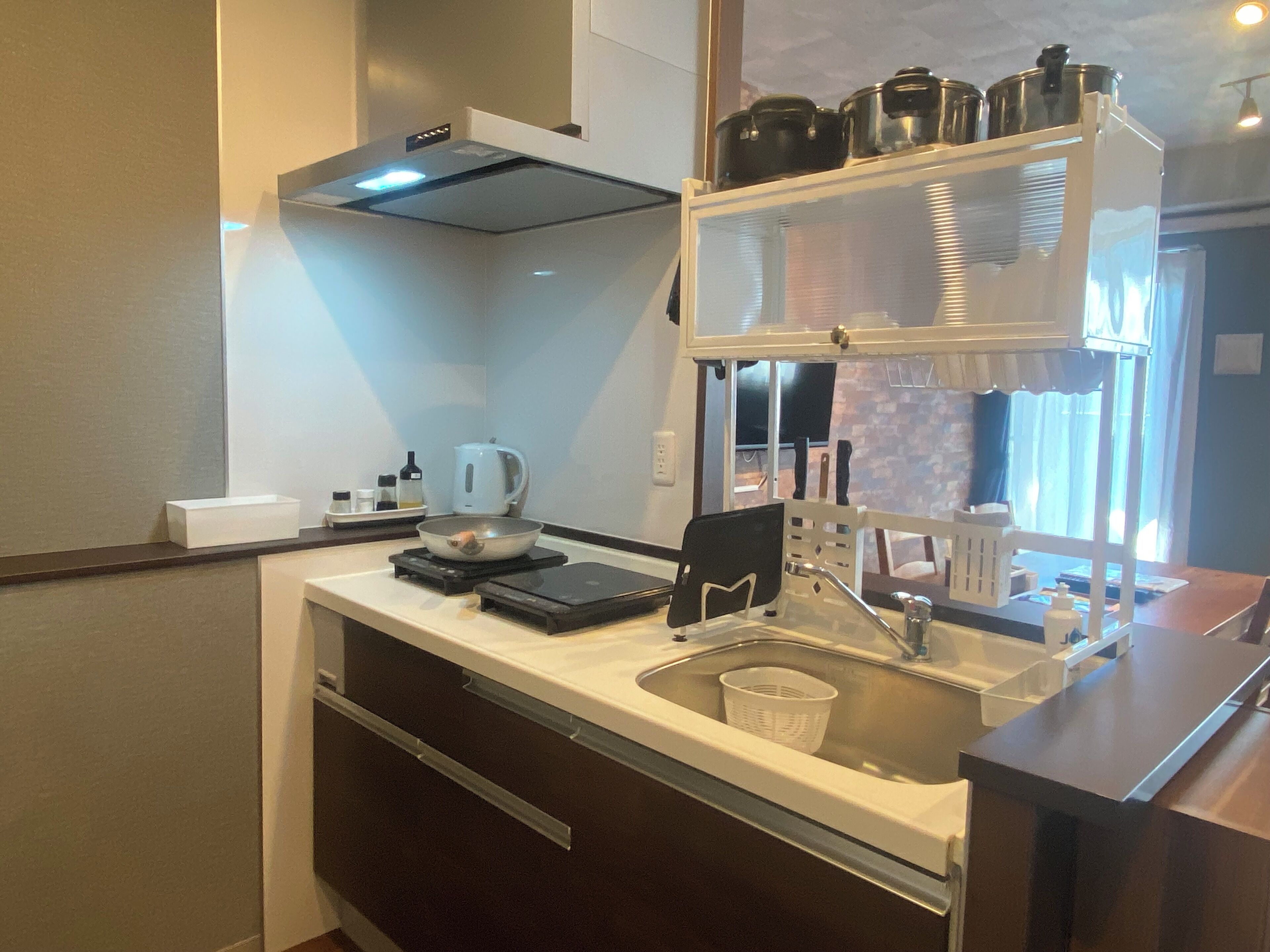 A compact kitchen with a stove, kettle, and a shelf with pots.