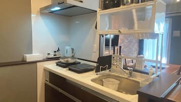 A compact kitchen with a stove, kettle, and a shelf with pots.