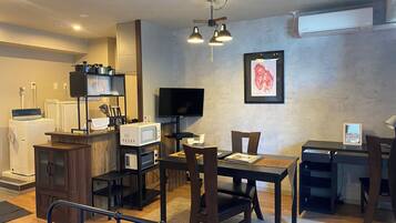 A compact living space with a kitchenette, a dining area, a TV mounted on the wall, and a framed artwork.