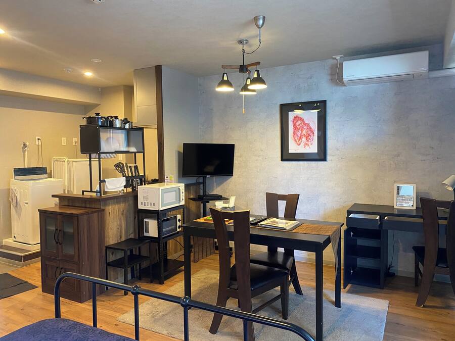 A compact living space with a kitchenette, a dining area, a TV mounted on the wall, and a framed artwork.